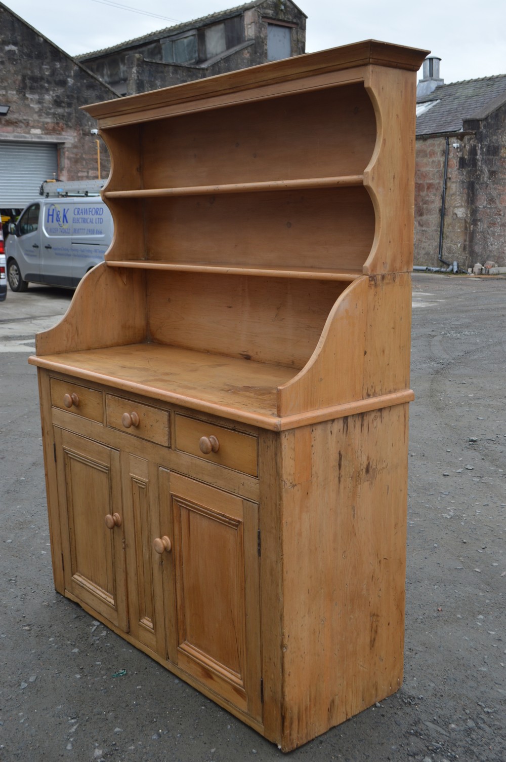 A Victorian Scots pine dresser featuring an upper open-shelf display rack above a base with three drawers and lower double cupboard doors. View V