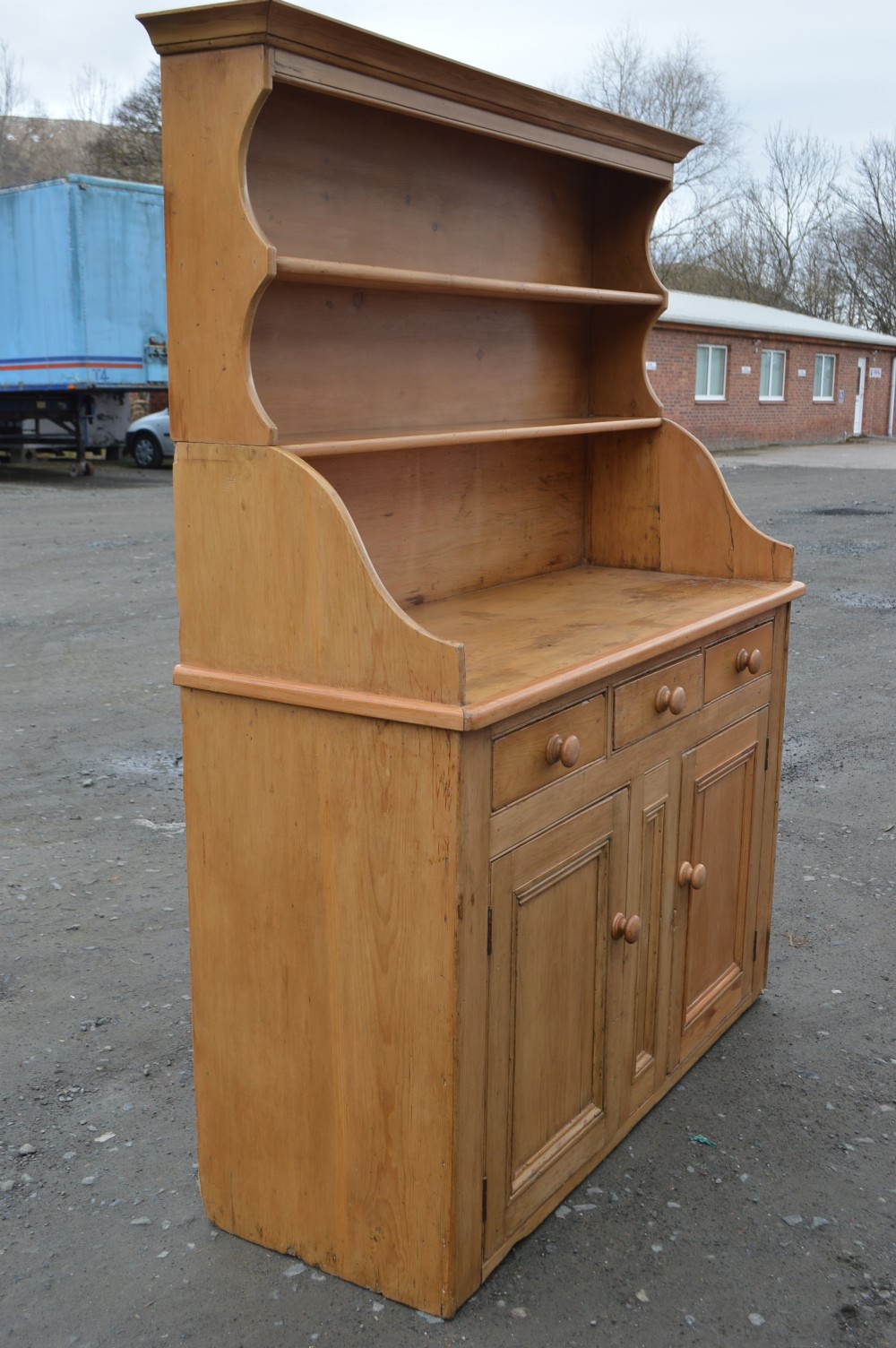 A Victorian Scots pine dresser featuring an upper open-shelf display rack above a base with three drawers and lower double cupboard doors. View VI