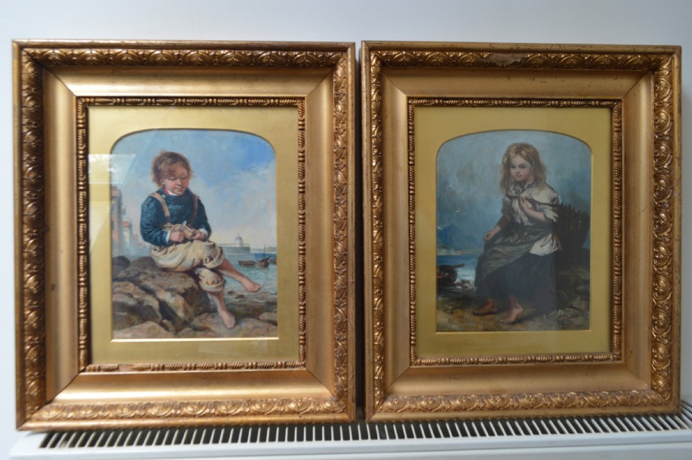 A pair of framed Scottish oil paintings depicting coastal children seated outdoors set within gilded frames.