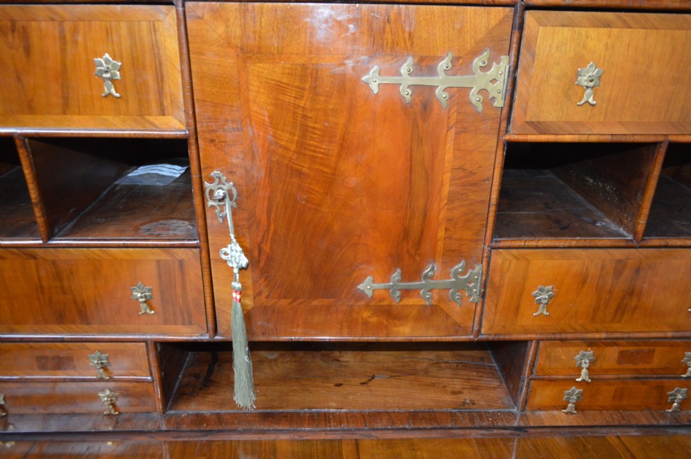 A George II walnut escritoire desk featuring an upper cabinet with pigeonholes and small drawers above a writing table base with brass handles. View V