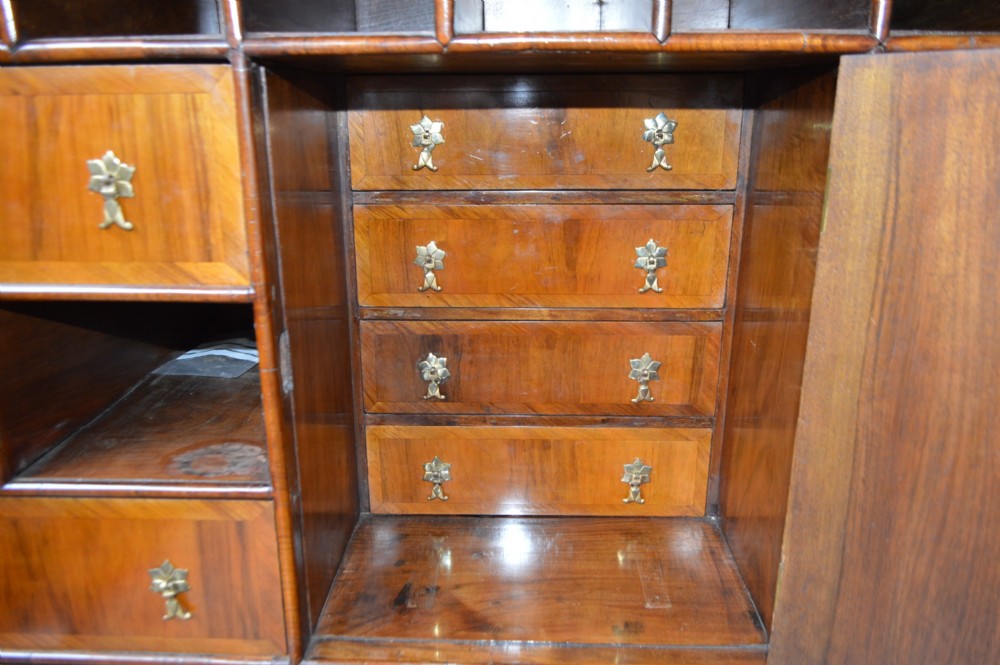 A George II walnut escritoire desk featuring an upper cabinet with pigeonholes and small drawers above a writing table base with brass handles. View VI