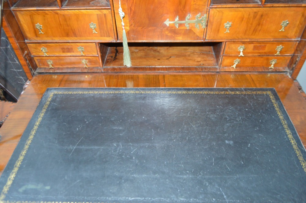 A George II walnut escritoire desk featuring an upper cabinet with pigeonholes and small drawers above a writing table base with brass handles. View VII