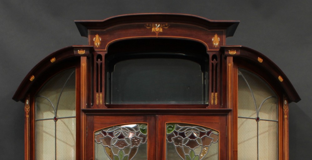 An Art Nouveau mahogany display cabinet with leaded glass doors, floral marquetry inlays, and flanking vitrine sections. View IV