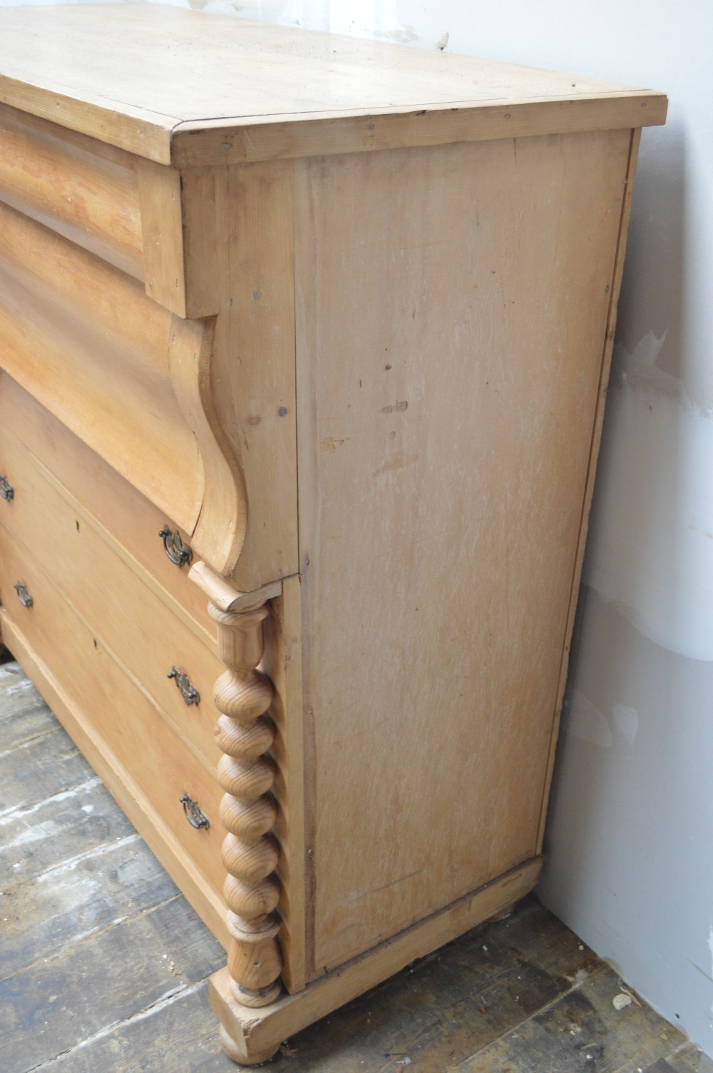 A Victorian pine chest of drawers featuring an ogee top drawer, turned side columns, brass handles, and bun feet. View IV