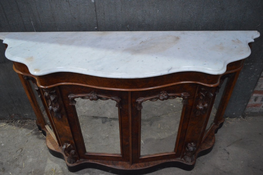A Victorian serpentine burr walnut credenza featuring a white shaped marble top, four mirrored doors, and carved foliate pilasters. View II
