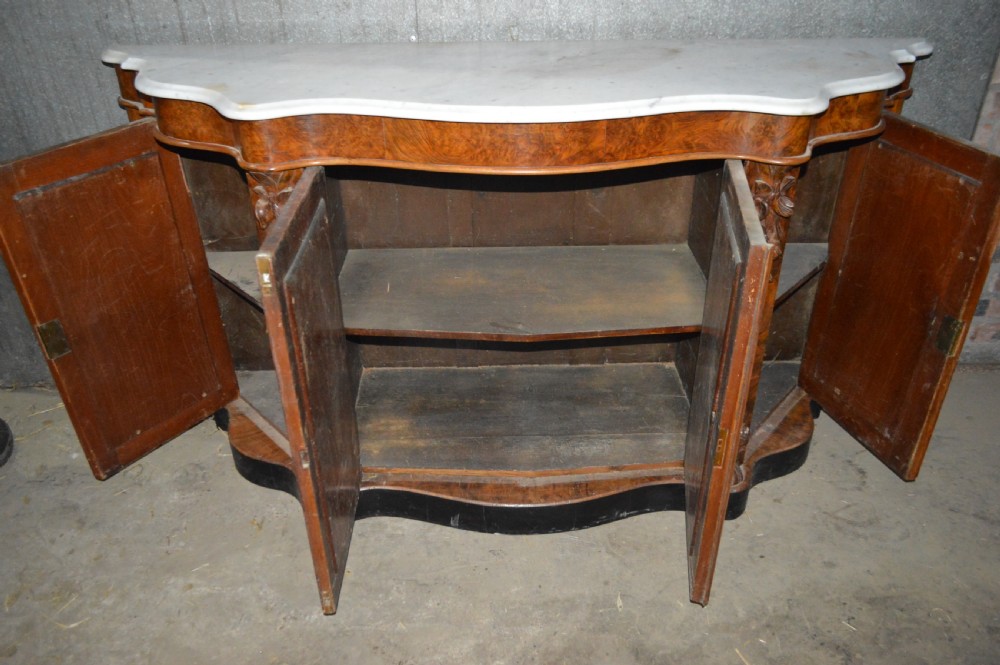A Victorian serpentine burr walnut credenza featuring a white shaped marble top, four mirrored doors, and carved foliate pilasters. View III