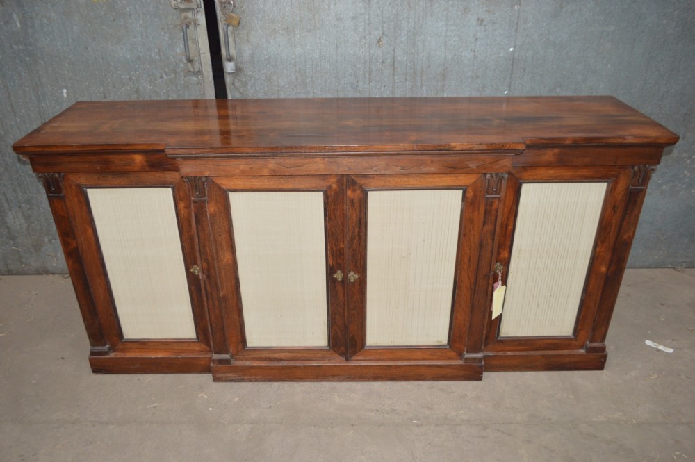 A Regency rosewood breakfront cabinet featuring four doors with pleated fabric panels and carved pilasters.