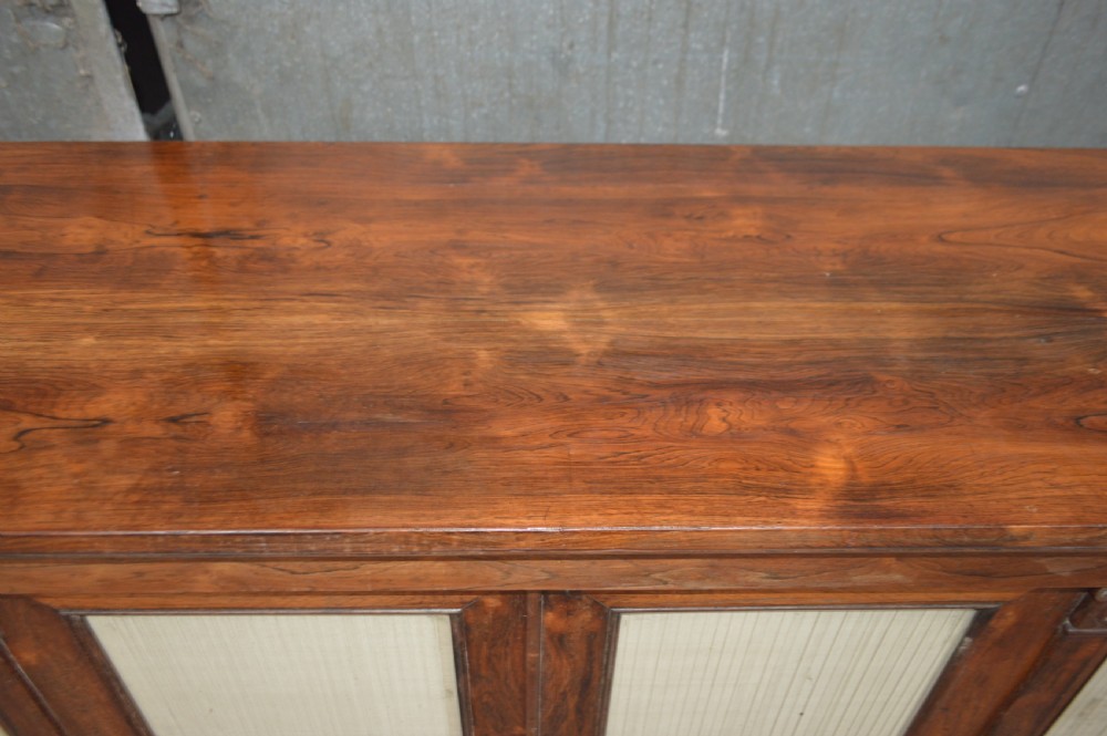 A Regency rosewood breakfront cabinet featuring four doors with pleated fabric panels and carved pilasters. View X