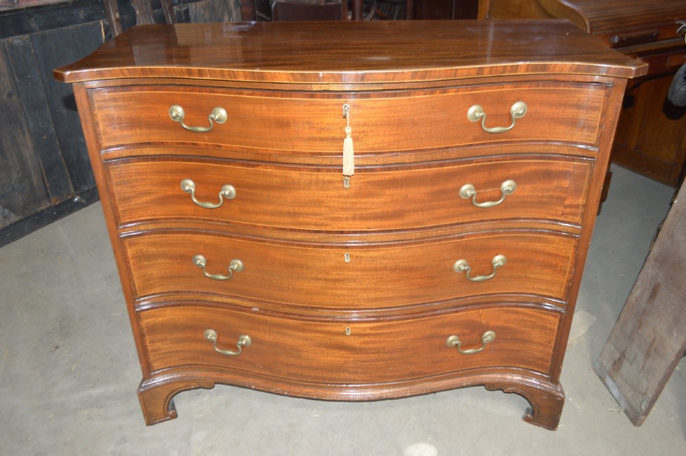 An 18th-century mahogany serpentine chest of drawers featuring four graduating drawers with brass handles and ogee bracket feet. View V