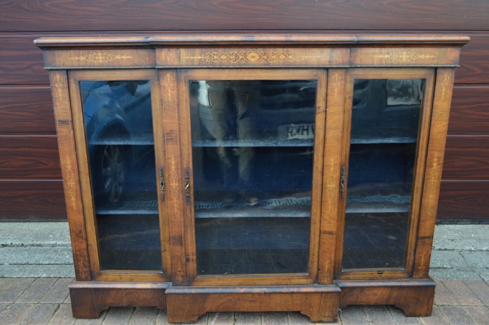 A low Victorian burr walnut breakfront bookcase featuring three glazed doors with floral marquetry inlays and decorative metal escutcheons.
