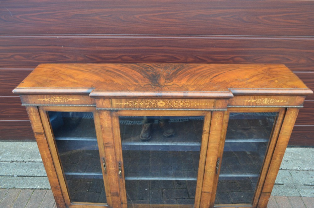 A low Victorian burr walnut breakfront bookcase featuring three glazed doors with floral marquetry inlays and decorative metal escutcheons. View II