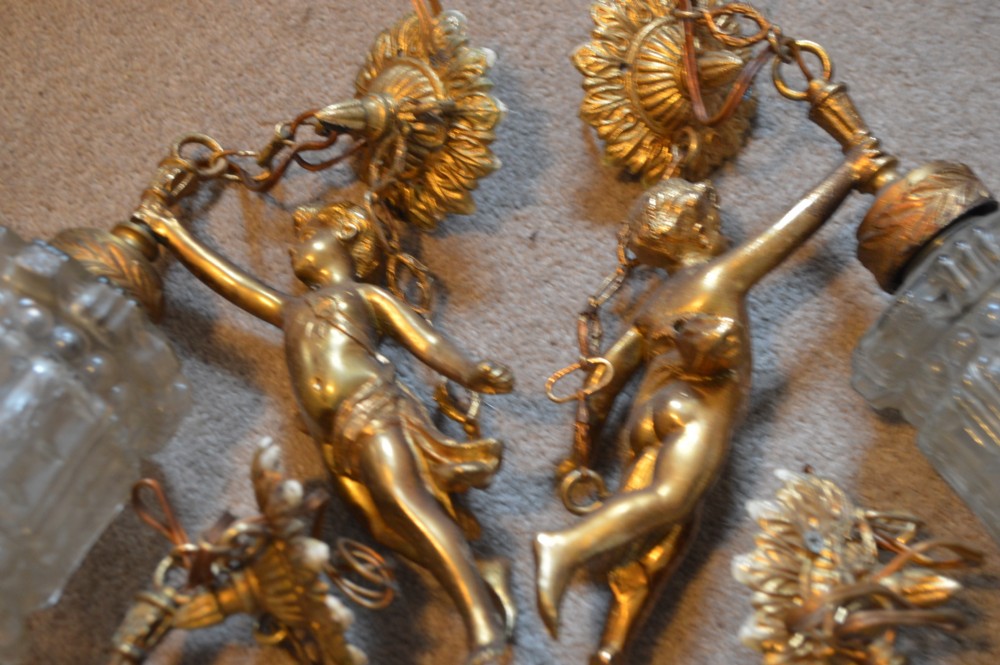 A set of four gilt metal light fittings depicting flying cherubs holding textured clear glass shades. View II