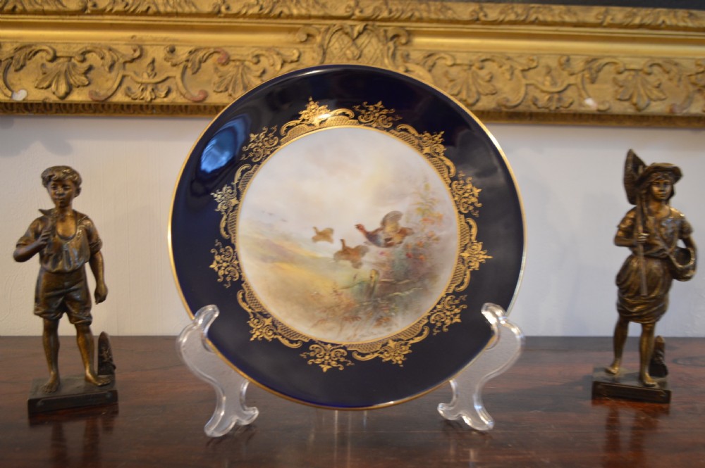 A circular Royal Worcester porcelain cabinet plate featuring a central hand-painted scene of game birds in flight surrounded by a dark cobalt blue rim with gold scrollwork gilding.
