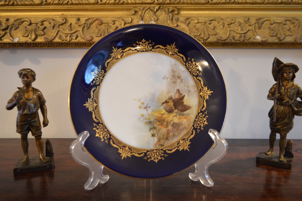 A circular Royal Worcester porcelain cabinet plate featuring a central hand-painted scene of game birds in flight surrounded by a dark cobalt blue rim with gold scrollwork gilding. View V
