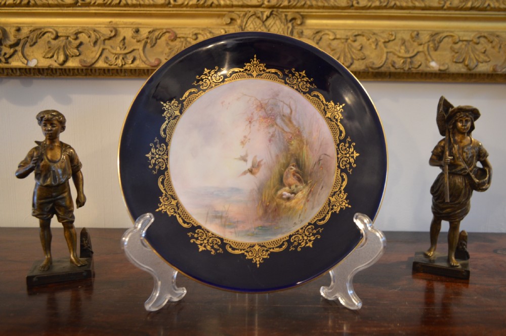 A circular Royal Worcester porcelain cabinet plate featuring a central hand-painted scene of game birds in flight surrounded by a dark cobalt blue rim with gold scrollwork gilding. View VII