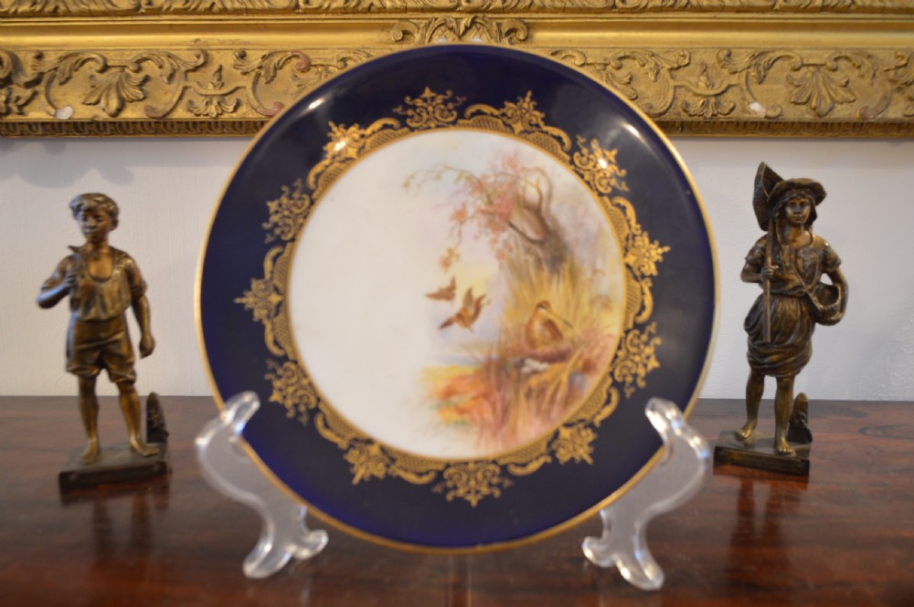 A circular Royal Worcester porcelain cabinet plate featuring a central hand-painted scene of game birds in flight surrounded by a dark cobalt blue rim with gold scrollwork gilding. View XV