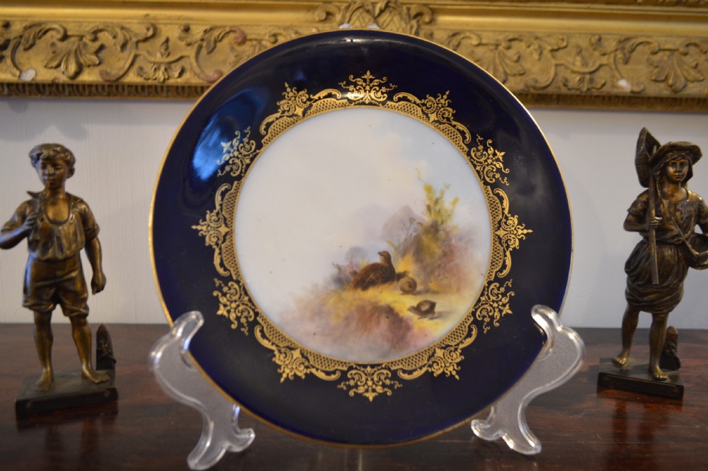A circular Royal Worcester porcelain cabinet plate featuring a central hand-painted scene of game birds in flight surrounded by a dark cobalt blue rim with gold scrollwork gilding. View XXIII