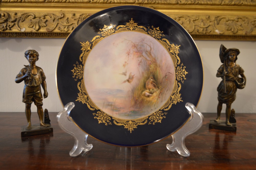 A circular Royal Worcester porcelain cabinet plate featuring a central hand-painted scene of game birds in flight surrounded by a dark cobalt blue rim with gold scrollwork gilding. View X