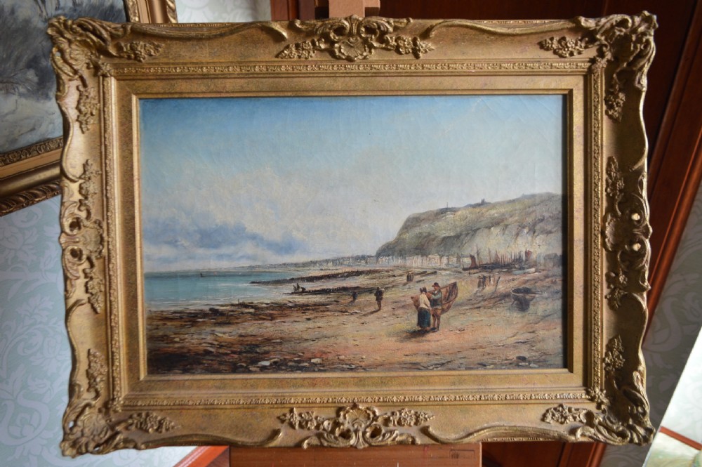 A 19th-century coastal oil painting depicting figures on a beach near cliffs, housed in an ornate giltwood frame.