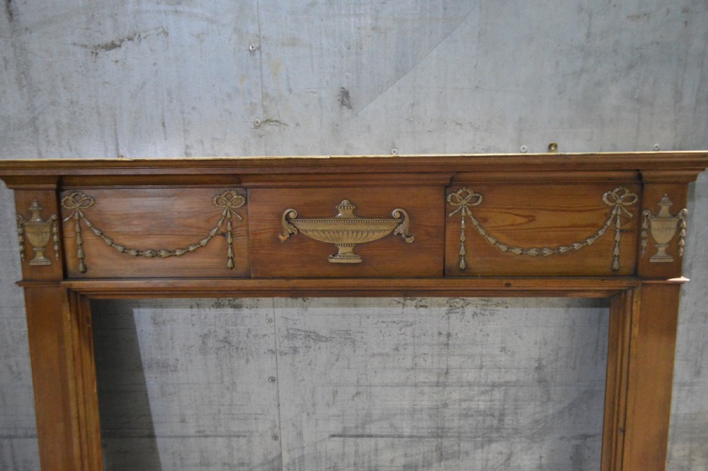 A Regency period pine fire surround featuring detailed gesso classical urns, draped swags, and fluted jambs. View II