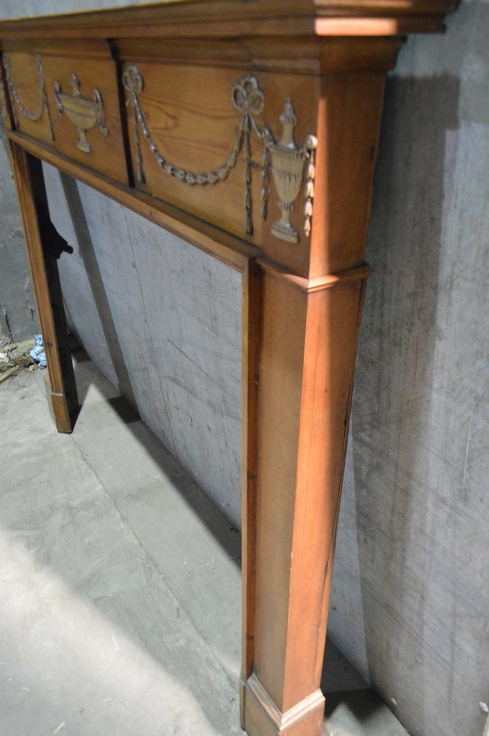 A Regency period pine fire surround featuring detailed gesso classical urns, draped swags, and fluted jambs. View IV