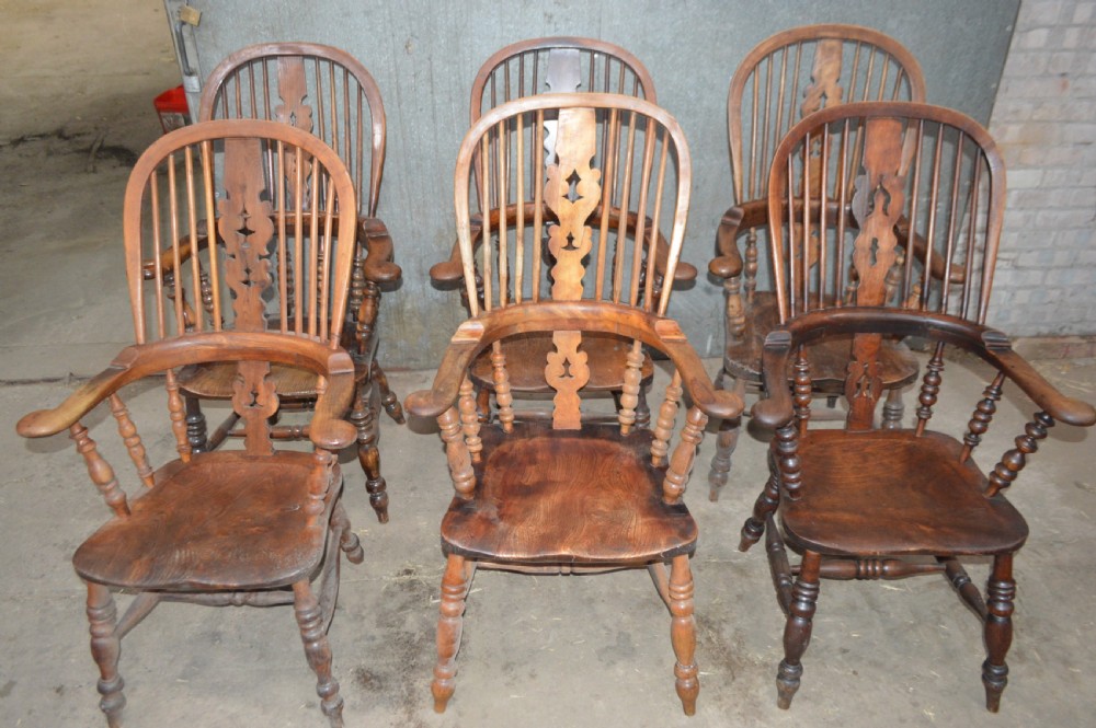 A set of six Victorian wooden Windsor armchairs featuring high hoop backs, central decorative splats, pad arms, and turned legs.