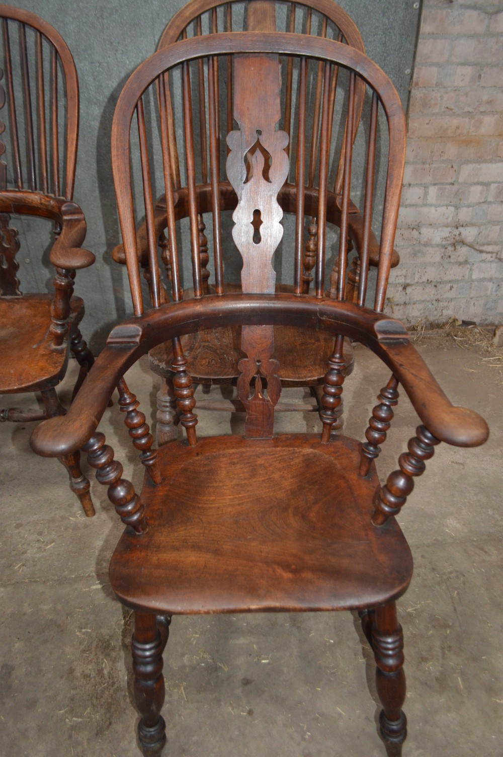 A set of six Victorian wooden Windsor armchairs featuring high hoop backs, central decorative splats, pad arms, and turned legs. View VI