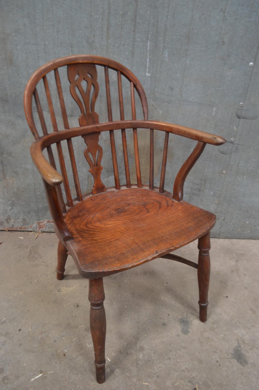A Victorian low back Windsor armchair crafted from warm brown wood, featuring a bentwood arm bow, turned legs, and a decorative central pierced splat.