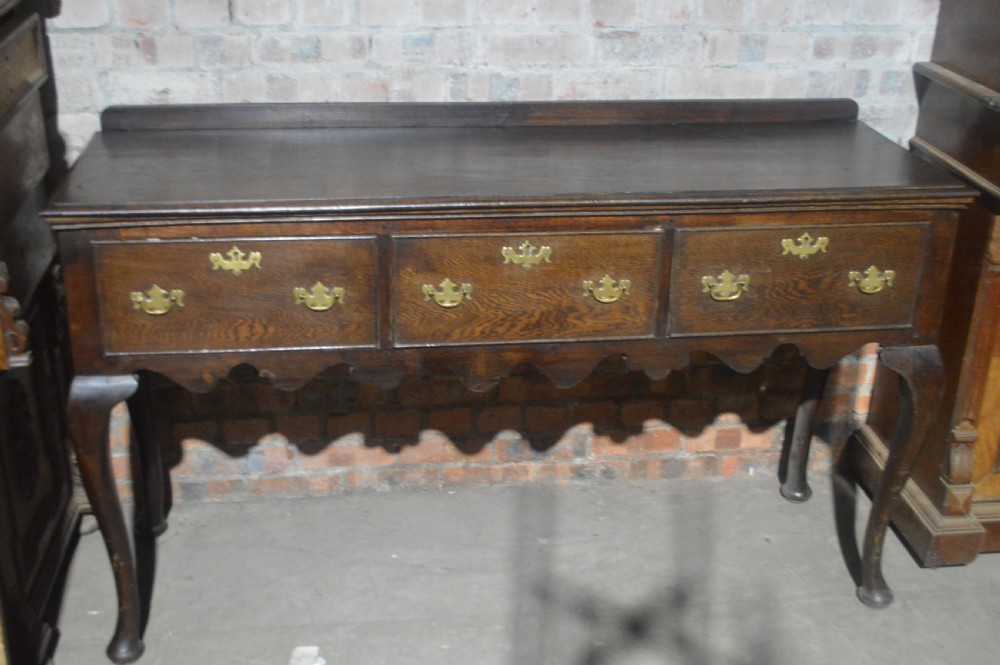 A dark oak Victorian dresser base featuring three drawers with brass handles, a scalloped lower apron, and slender cabriole legs.