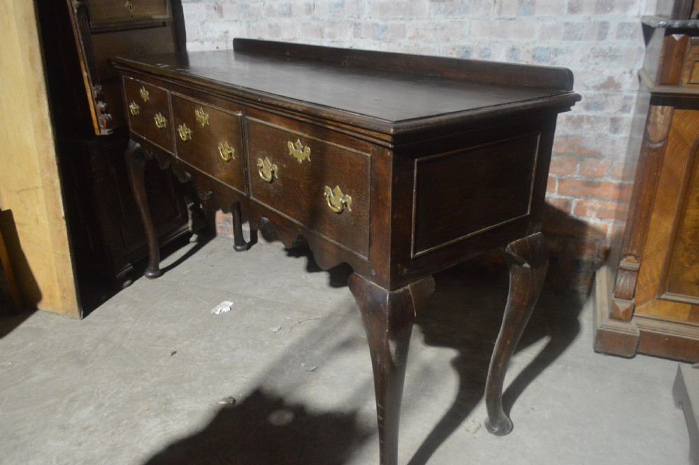 A dark oak Victorian dresser base featuring three drawers with brass handles, a scalloped lower apron, and slender cabriole legs. View II