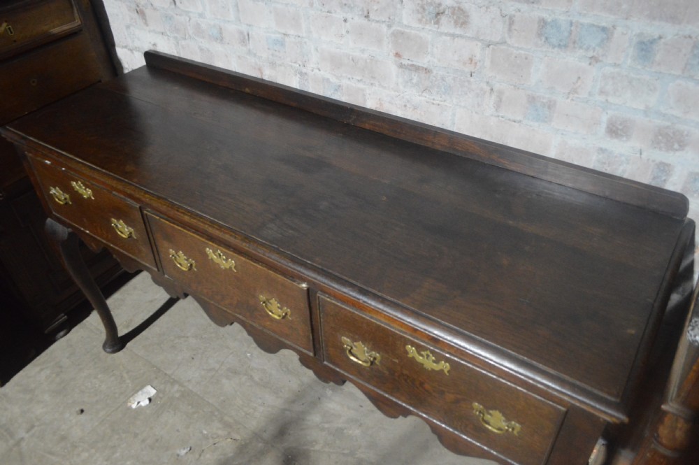 A dark oak Victorian dresser base featuring three drawers with brass handles, a scalloped lower apron, and slender cabriole legs. View III