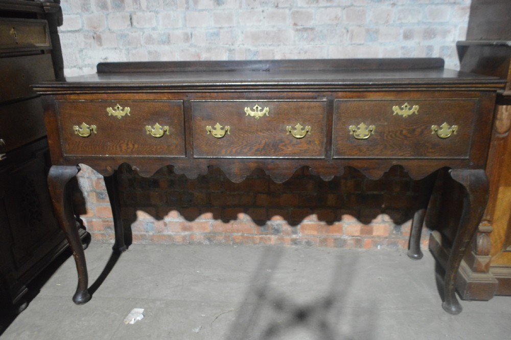 A dark oak Victorian dresser base featuring three drawers with brass handles, a scalloped lower apron, and slender cabriole legs. View IV