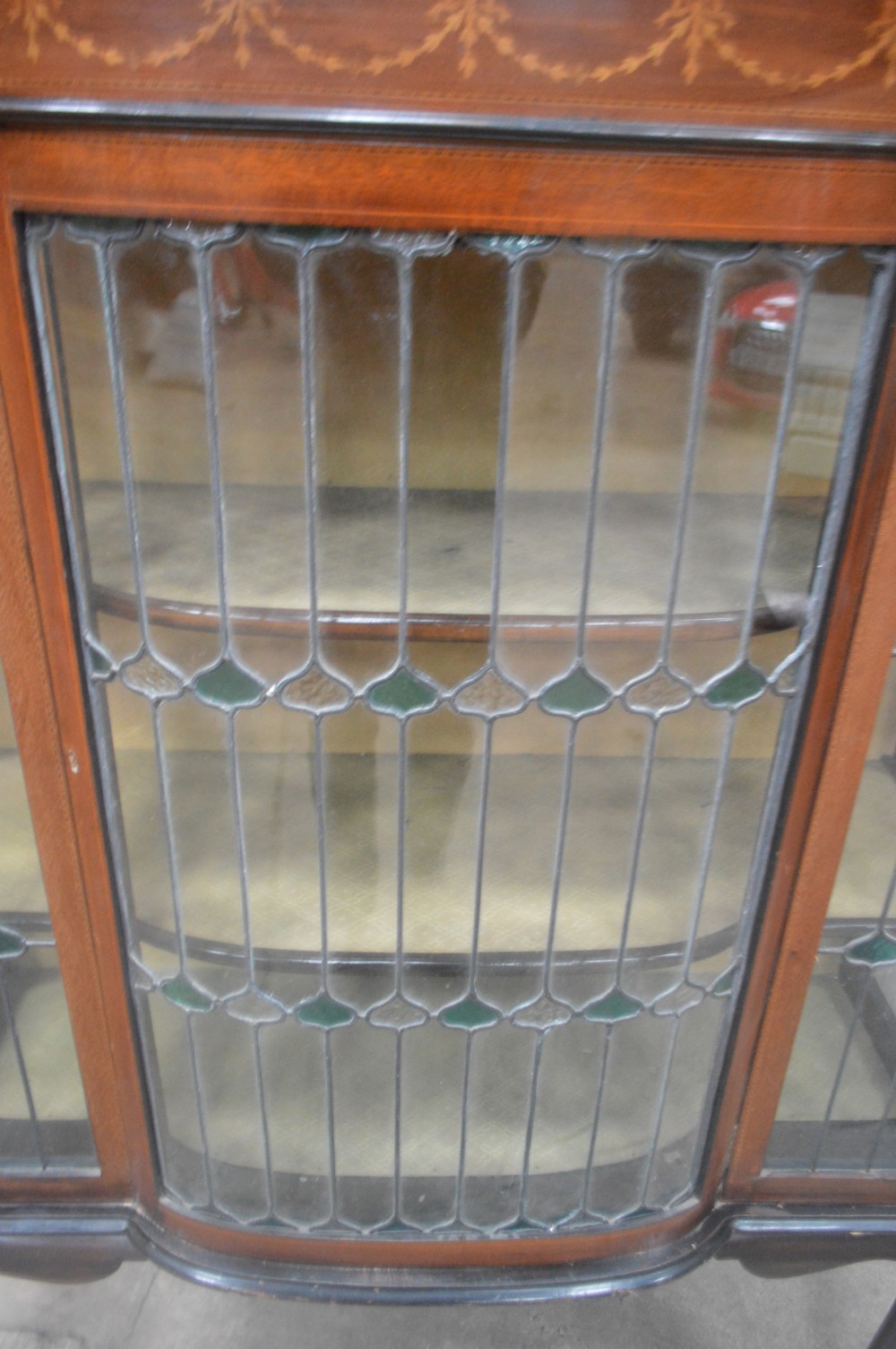 An Edwardian mahogany display cabinet featuring inlaid satinwood swags on the pediment, leaded glass doors with green accents, and slender cabriole legs. View II