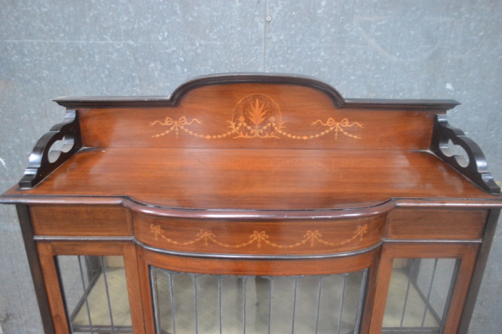 An Edwardian mahogany display cabinet featuring inlaid satinwood swags on the pediment, leaded glass doors with green accents, and slender cabriole legs. View III