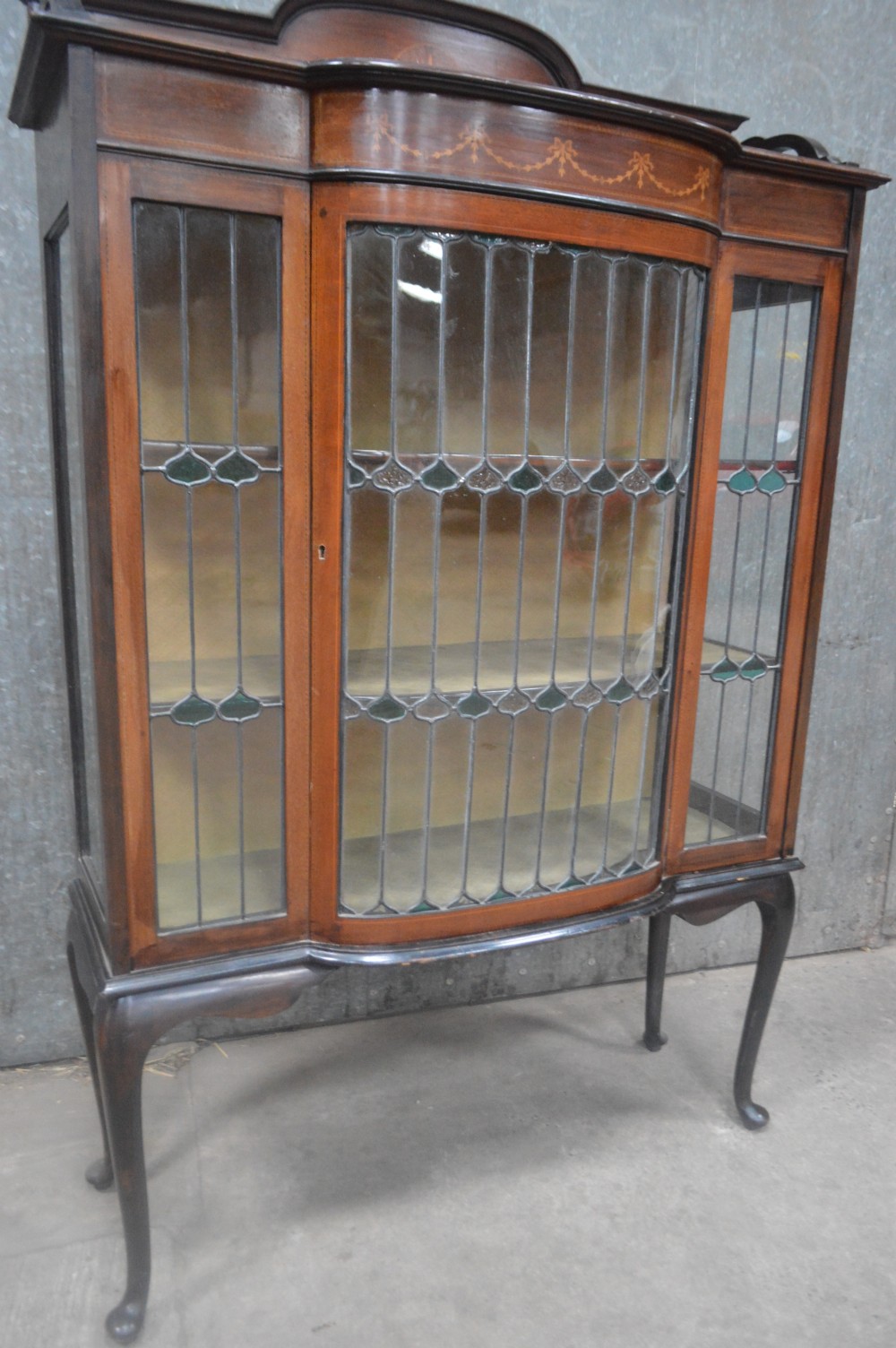 An Edwardian mahogany display cabinet featuring inlaid satinwood swags on the pediment, leaded glass doors with green accents, and slender cabriole legs. View V