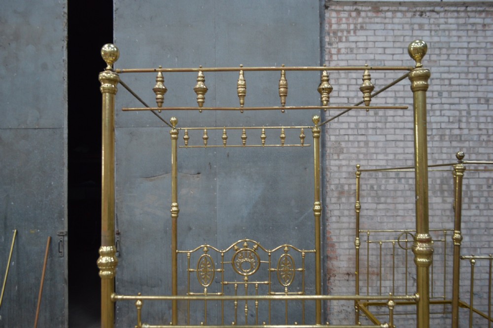A Victorian tubular brass four poster bed frame featuring decorative spindled canopy rails, turned finials, and an ornamental central headboard motif. View III