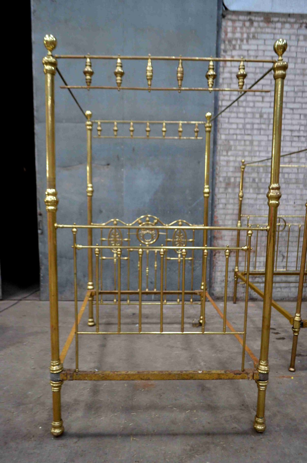 A Victorian tubular brass four poster bed frame featuring decorative spindled canopy rails, turned finials, and an ornamental central headboard motif.