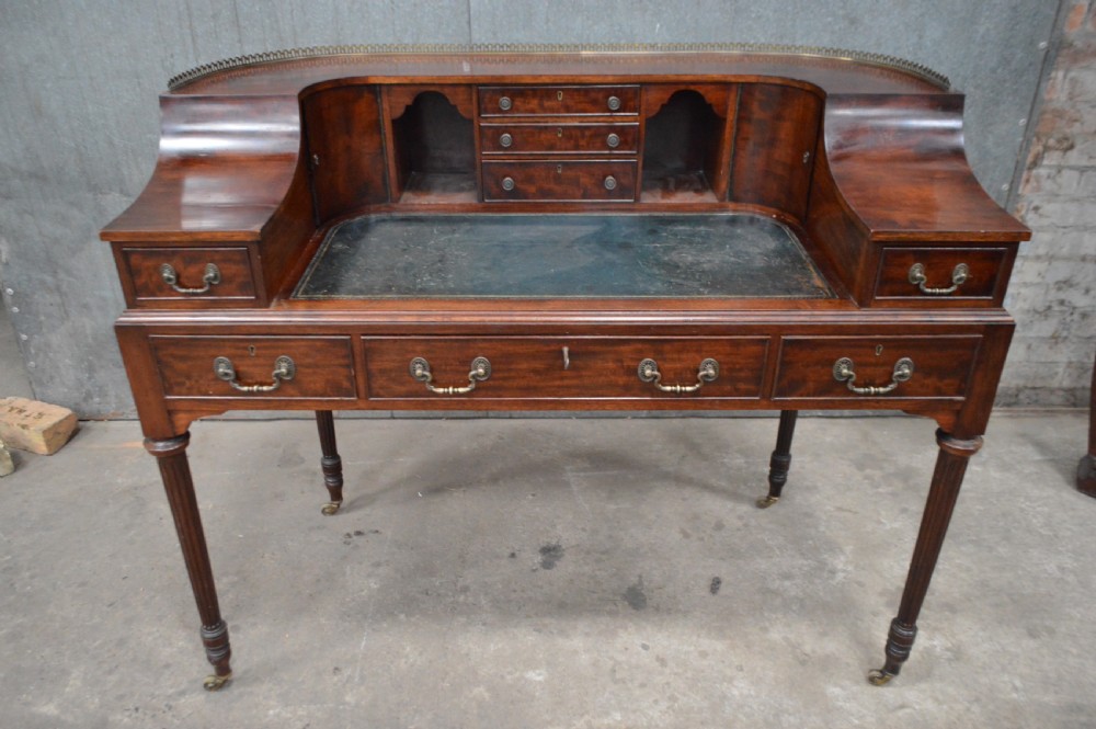 An Edwardian mahogany Carlton House writing desk featuring a curved U-shaped superstructure with small drawers, pigeonholes, a brass gallery, a dark leather insert, and fluted legs on brass castors.