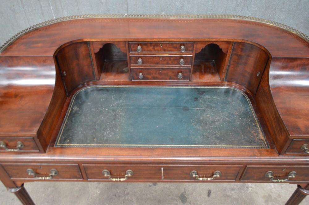 An Edwardian mahogany Carlton House writing desk featuring a curved U-shaped superstructure with small drawers, pigeonholes, a brass gallery, a dark leather insert, and fluted legs on brass castors. View II