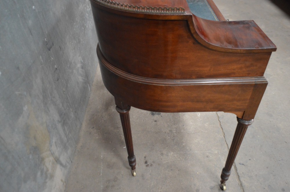 An Edwardian mahogany Carlton House writing desk featuring a curved U-shaped superstructure with small drawers, pigeonholes, a brass gallery, a dark leather insert, and fluted legs on brass castors. View III