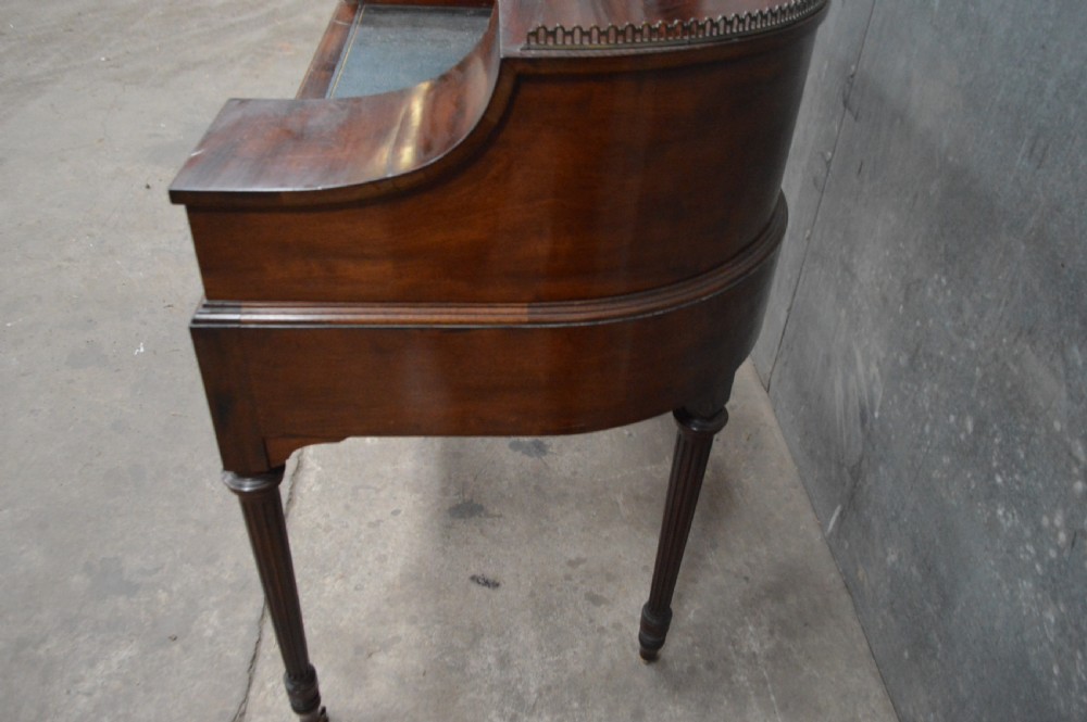 An Edwardian mahogany Carlton House writing desk featuring a curved U-shaped superstructure with small drawers, pigeonholes, a brass gallery, a dark leather insert, and fluted legs on brass castors. View V