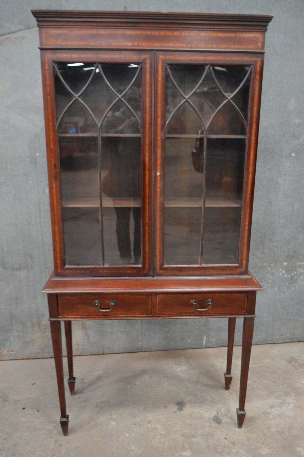 An Edwardian inlaid mahogany bookcase featuring two glazed doors with gothic astragal glazing, a two-drawer base, and square tapered legs.
