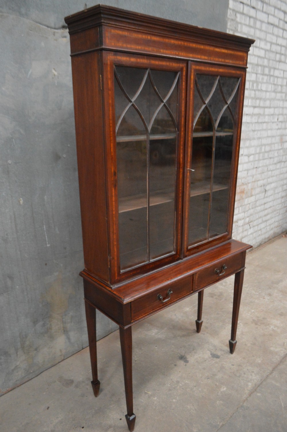 An Edwardian inlaid mahogany bookcase featuring two glazed doors with gothic astragal glazing, a two-drawer base, and square tapered legs. View II