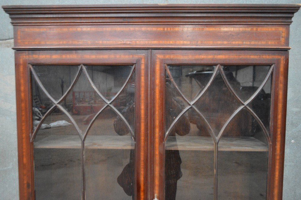 An Edwardian inlaid mahogany bookcase featuring two glazed doors with gothic astragal glazing, a two-drawer base, and square tapered legs. View III