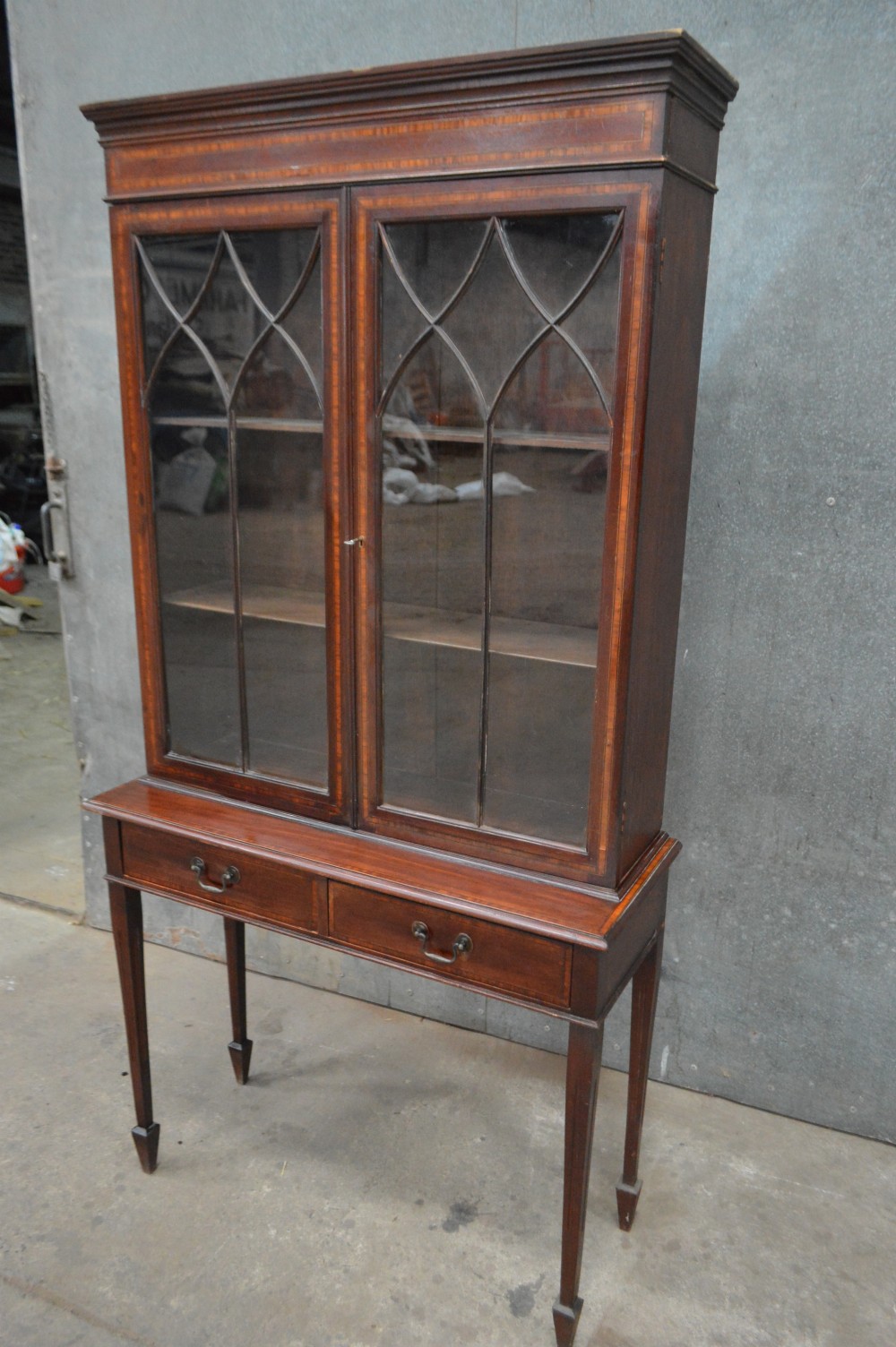An Edwardian inlaid mahogany bookcase featuring two glazed doors with gothic astragal glazing, a two-drawer base, and square tapered legs. View V