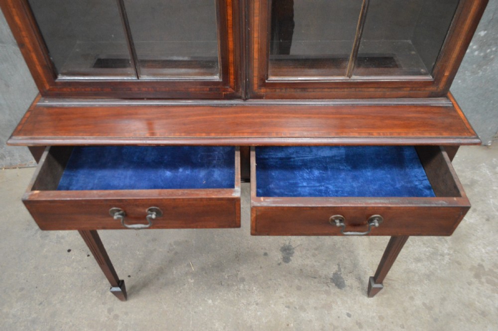 An Edwardian inlaid mahogany bookcase featuring two glazed doors with gothic astragal glazing, a two-drawer base, and square tapered legs. View VI