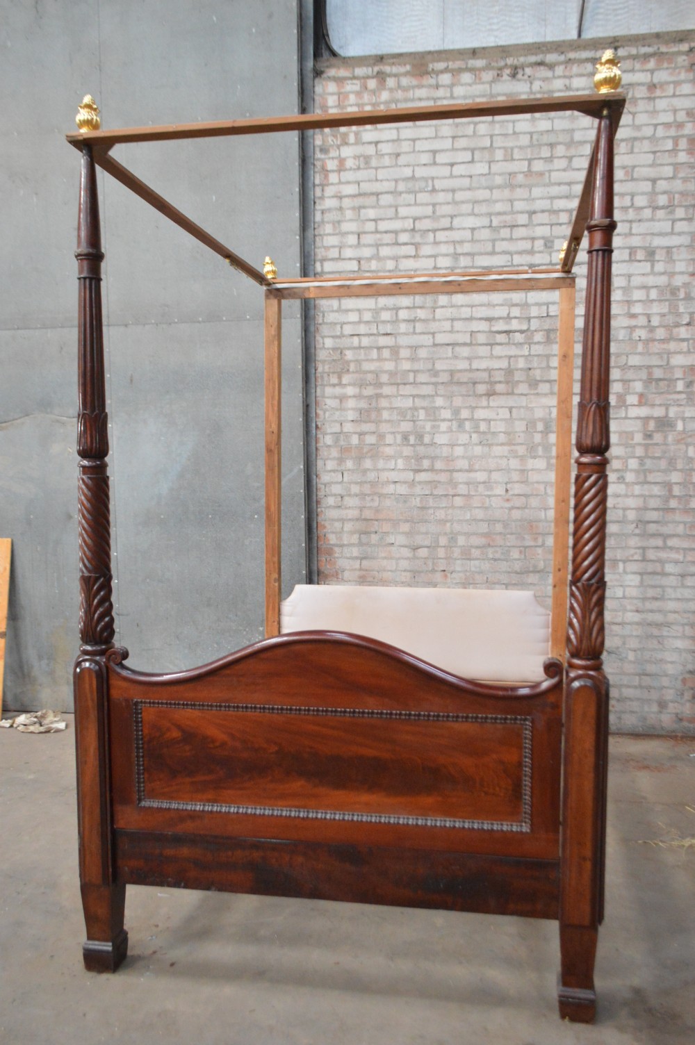 Victorian mahogany four poster bed featuring carved spiral posts, gilt finials, and an arched panelled footboard.