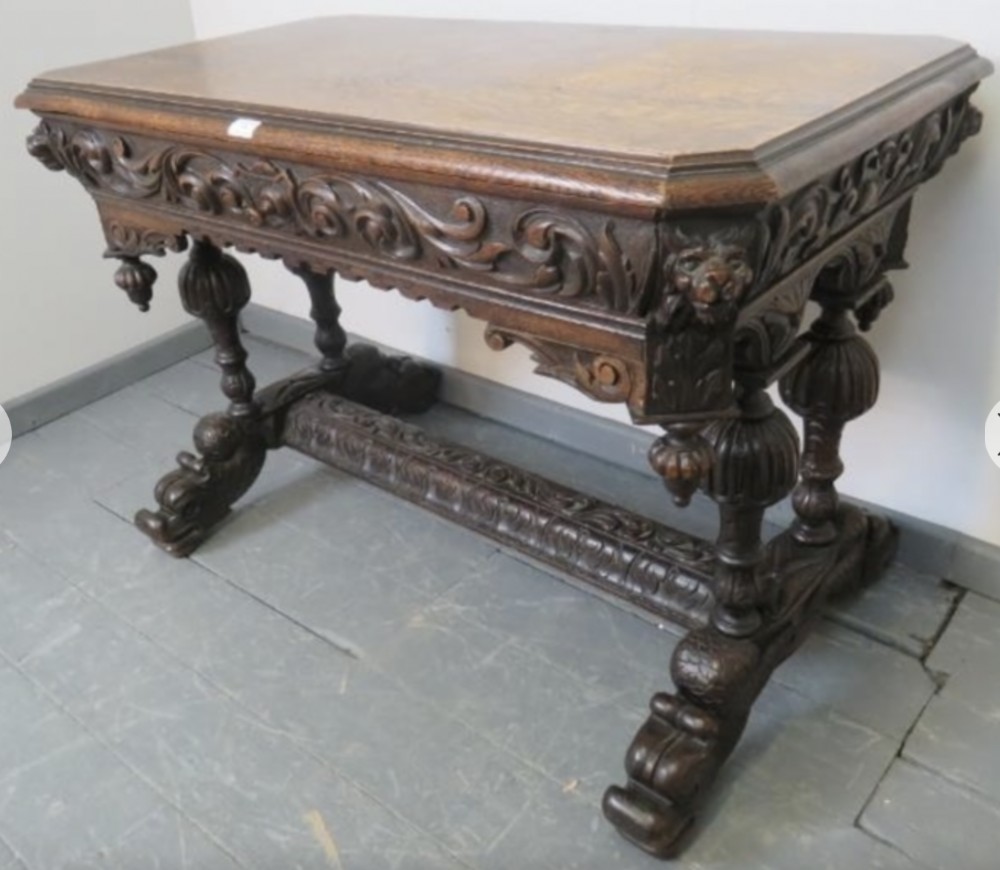 An antique dark oak console table featuring elaborate relief carvings along the frieze, lion mask corners, and heavily turned legs connected by a stretcher base.