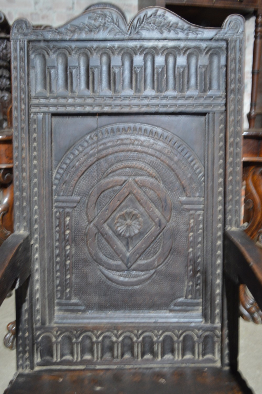 A dark carved oak wainscot armchair featuring a detailed arched panel back, turned front legs, and sturdy stretchers. View II