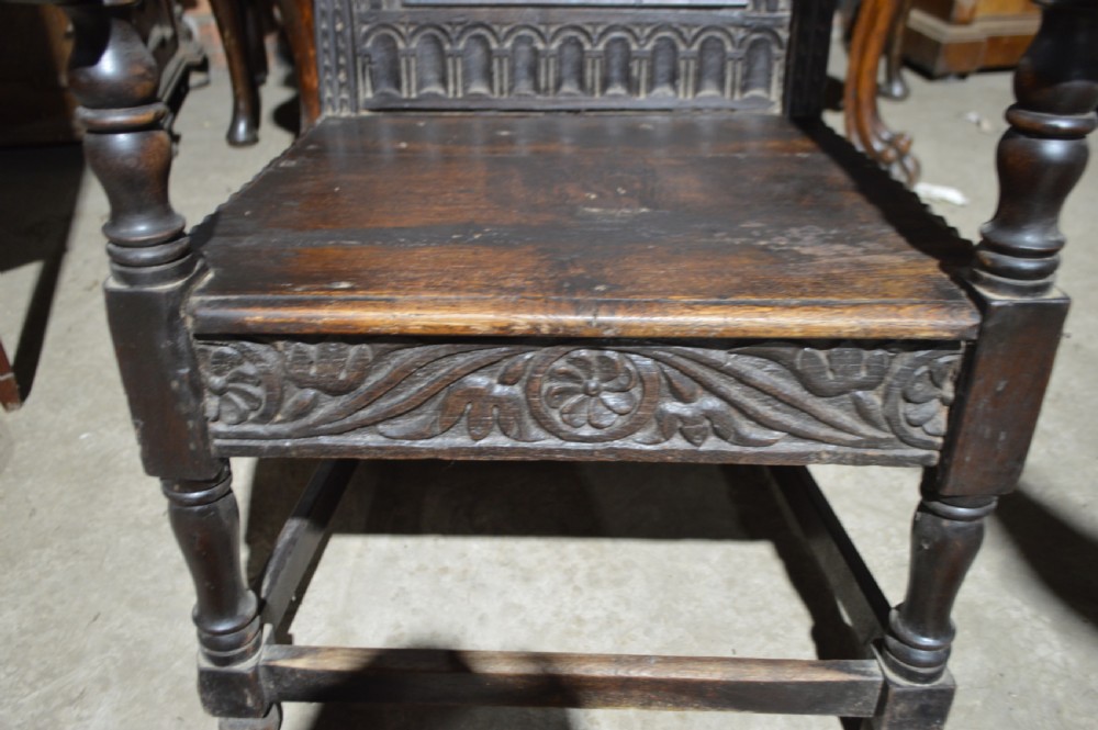 A dark carved oak wainscot armchair featuring a detailed arched panel back, turned front legs, and sturdy stretchers. View III